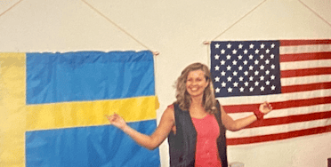 Pia Jansson standing between the Swedish and American flags smiling with arms raised. Pia Jansson Between Sweden and USA Flags